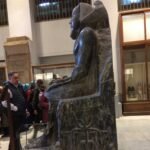 Древняя сидящая статуя тёмного камня в интерьере старого каирского музея среди экспонатов