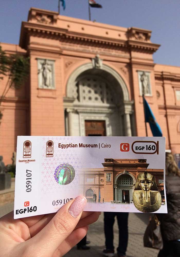 Билет в руке на фоне фасада каирского египетского музея и исторического здания