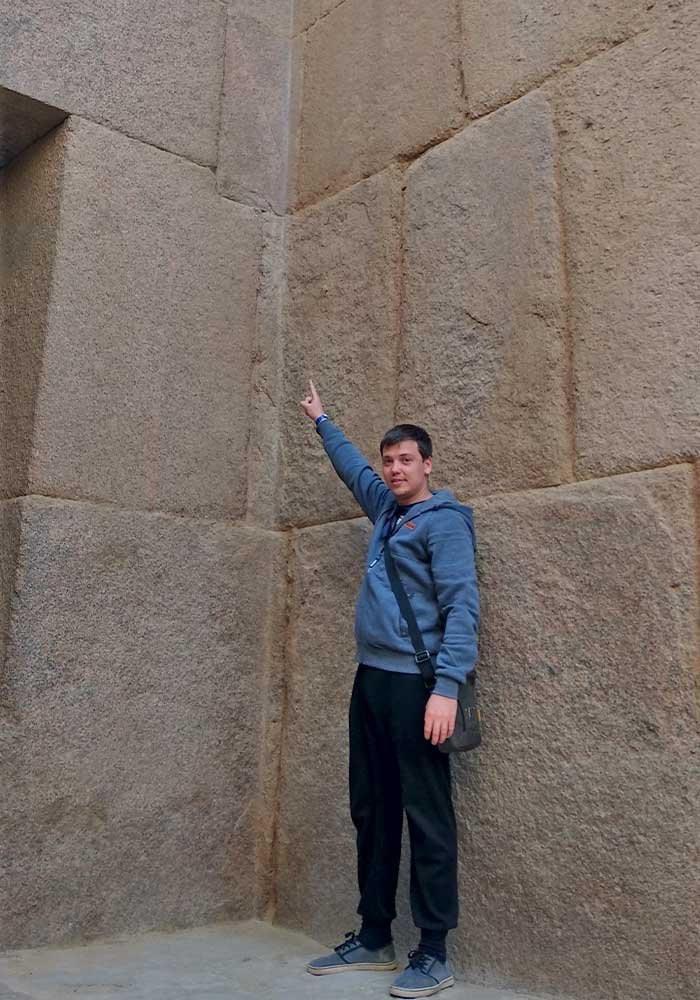Исследователь стоит возле гигантских гранитных блоков стены Храма Сфинкса демонстрируя размеры мегалитов